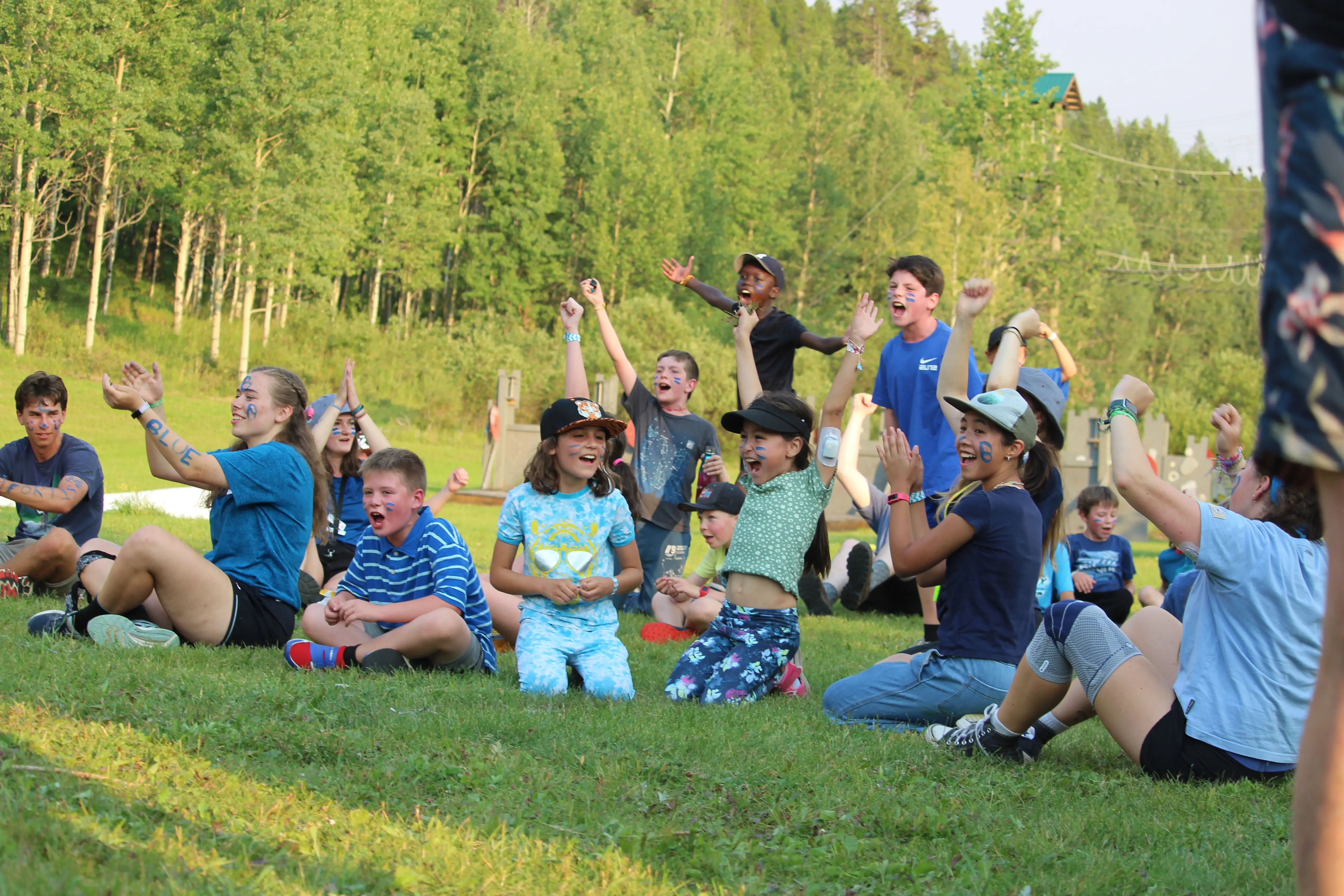 a group of kids sitting on grass with their hands up